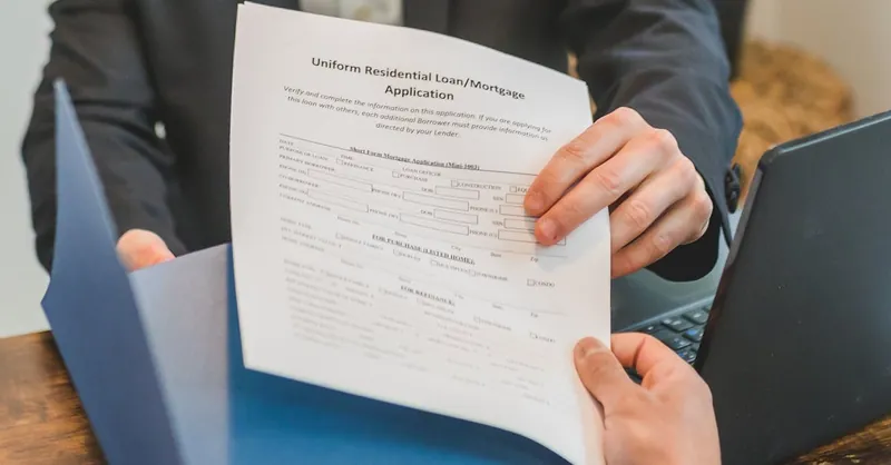 Professional setting showing hands exchanging a mortgage application document indoors.