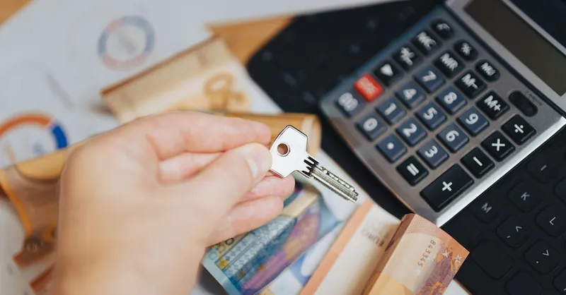 Hand holding key above Euro banknotes and calculator, symbolizing real estate investment.