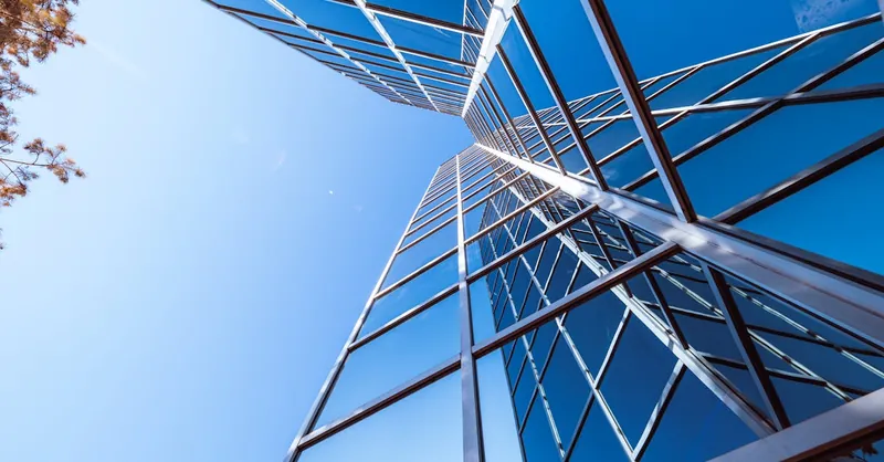 Low angle view of a modern skyscraper with a reflective glass facade against a clear blue sky.