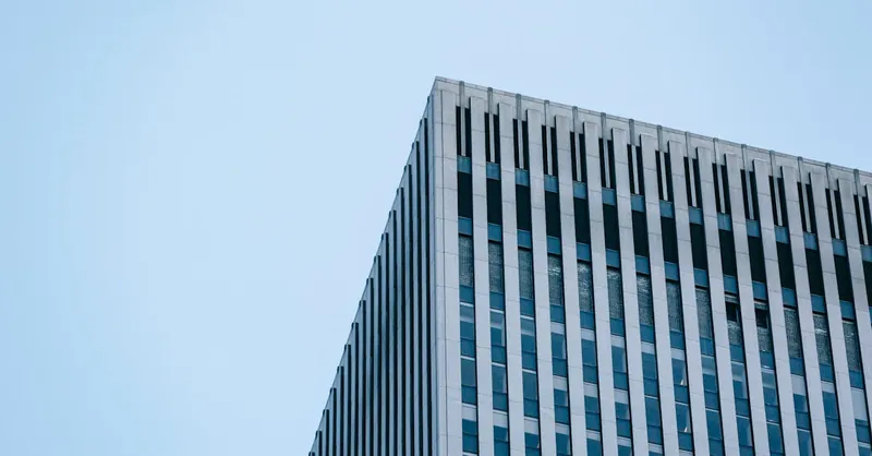 From below of geometric facade and corner of contemporary multistory commercial building against cloudless blue sky