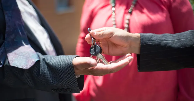 Close-up of two people exchanging keys, symbolizing real estate transaction.