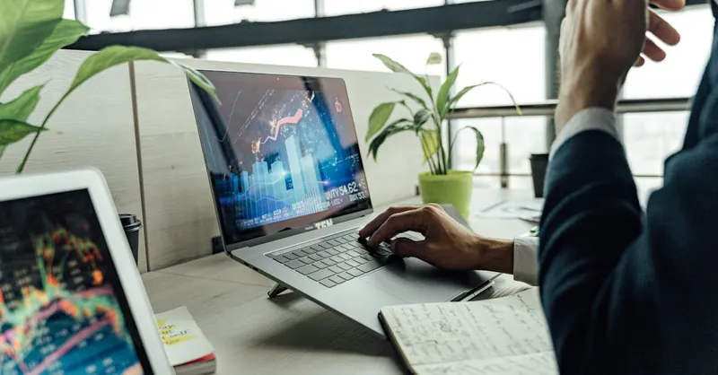 A professional analyzing stock market data on a laptop in a bright office environment.