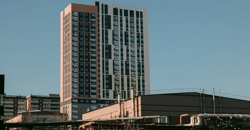 Low angle exterior of contemporary high rise residential building in urban district against cloudless blue sky