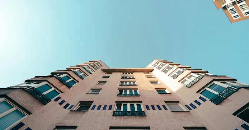 A modern residential building shot from a low angle under a bright blue sky.