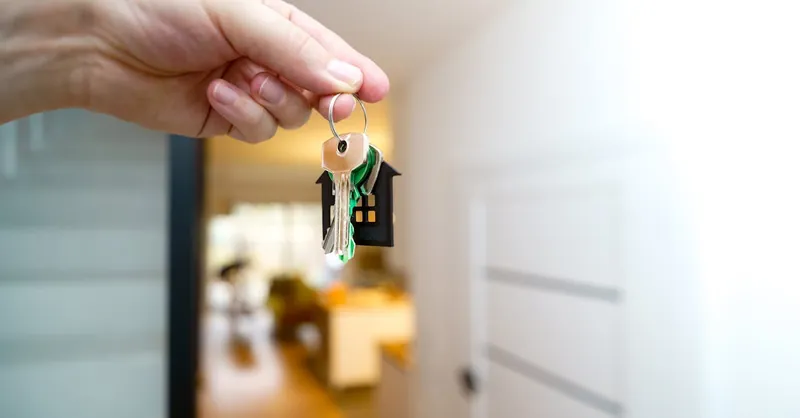 A hand holding house keys inside a modern apartment, symbolizing new property ownership or rental.
