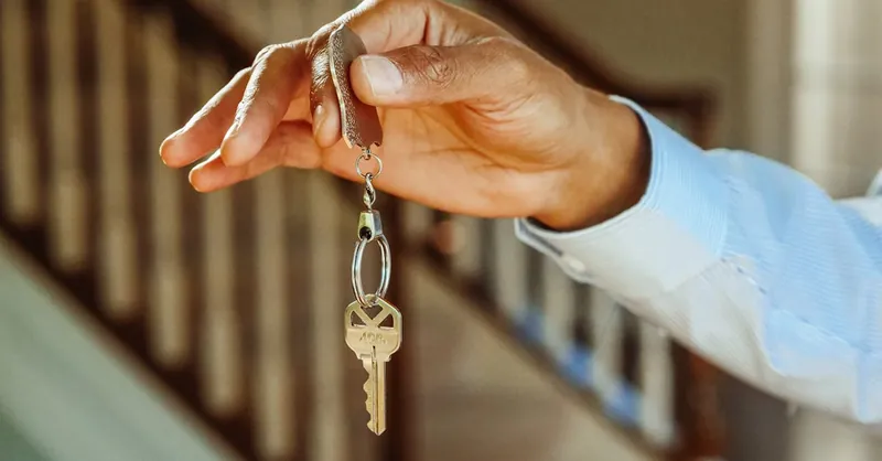 A close-up shot of a hand holding a house key, indicating new ownership or rental.