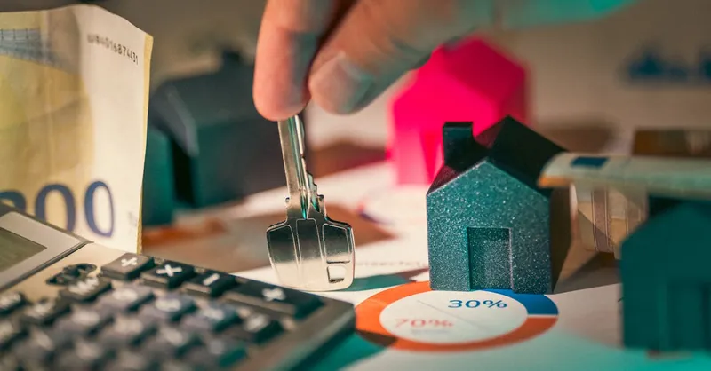 A close-up of real estate financial planning with keys, calculator, and money.