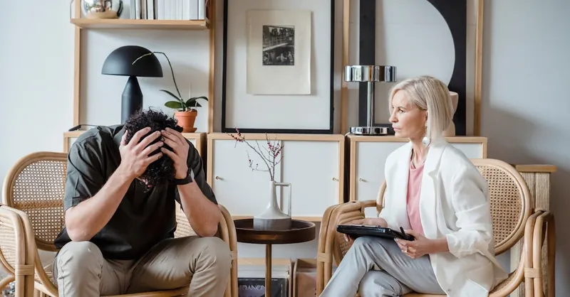 Professional therapy session with a stressed man and attentive female therapist in a modern office setting.