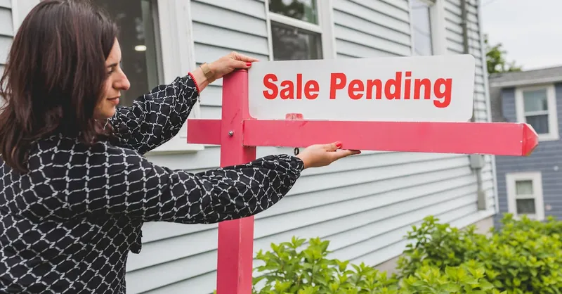 A realtor adjusting a sale pending sign outside a house for sale.