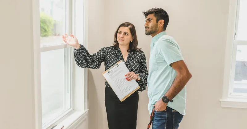 A real estate agent discusses property details with a client indoors, highlighting the view through large windows.