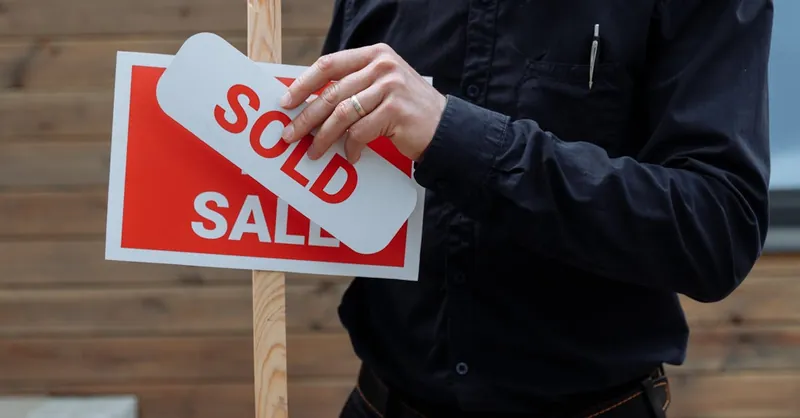 A real estate agent placing a sold sticker over a sale sign, indicating successful property deal.