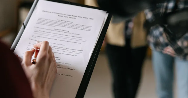 A couple examines real estate documents indoors with focus on writing and discussion.