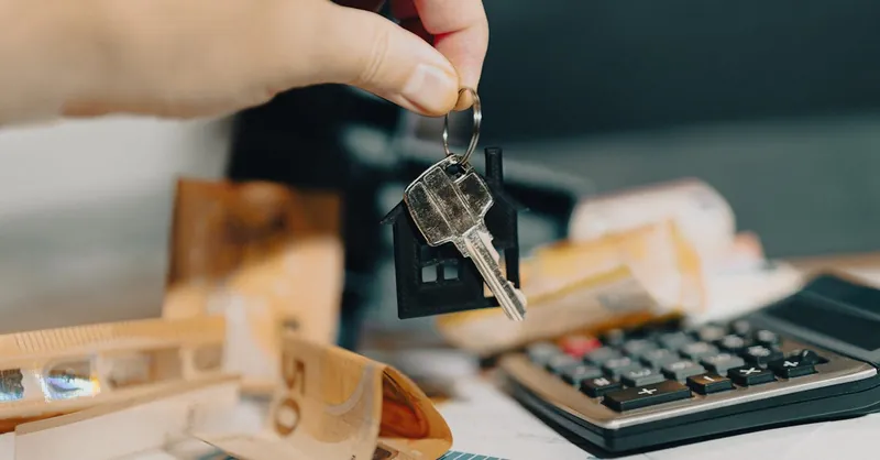 Close-up of a hand holding keys over euros and calculator, symbolizing real estate purchase.