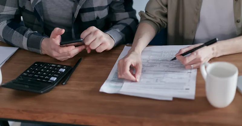 A couple diligently reviews their finances using a calculator and documents at home.