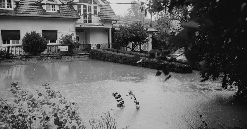 Black and white image of a suburban house affected by flooding during heavy rain.
