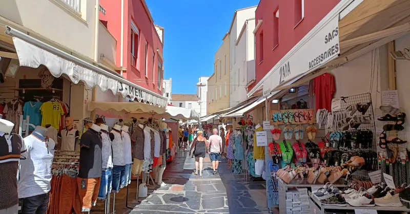 Vibrant summer market scene with shops, clothing displays and people walking.