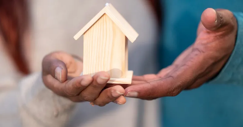 Close-up of hands holding a miniature wooden house, symbolizing home ownership and real estate investment.