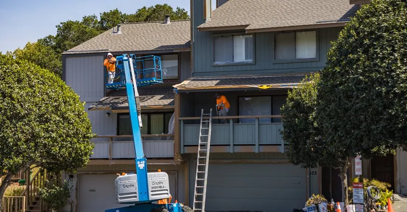 House being renovated with workers on a hydraulic lift in an urban area.