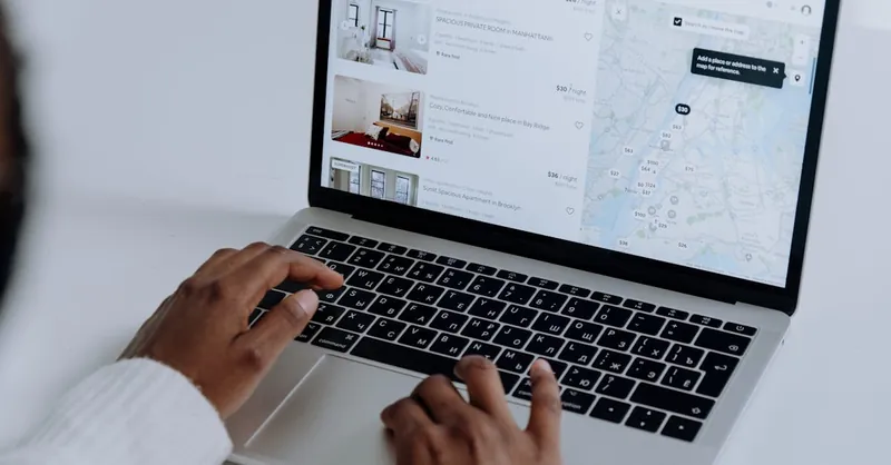 Hands typing on laptop searching Airbnb for accommodation options with map view.